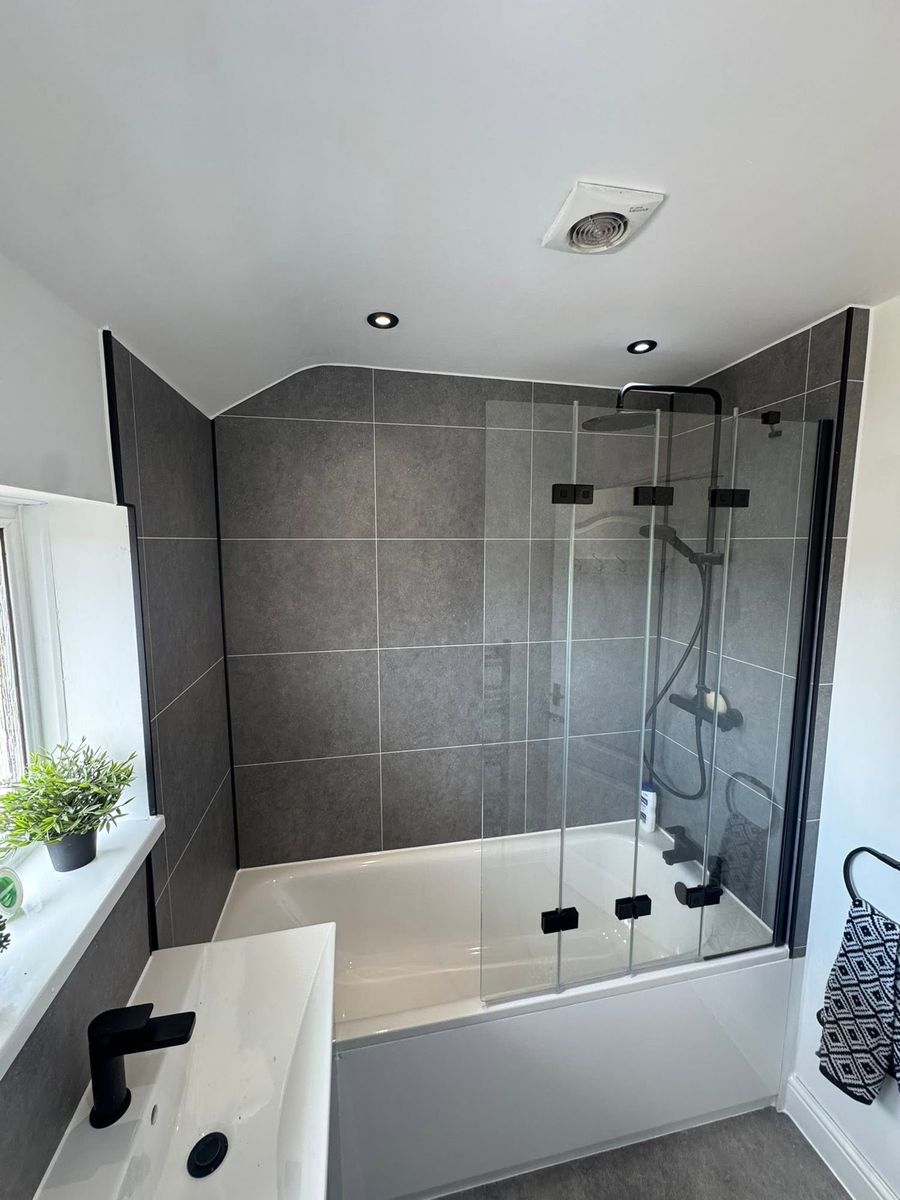 Grey tiled bathroom with a black-framed shower screen over the bath, fitted near Cullompton